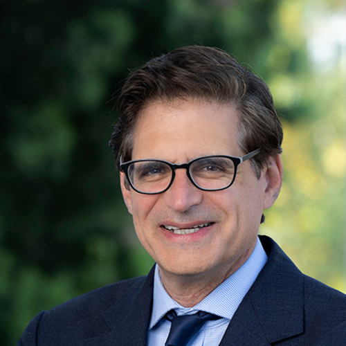 Josh Becker smiling in a professional headshot, wearing glasses and a navy suit