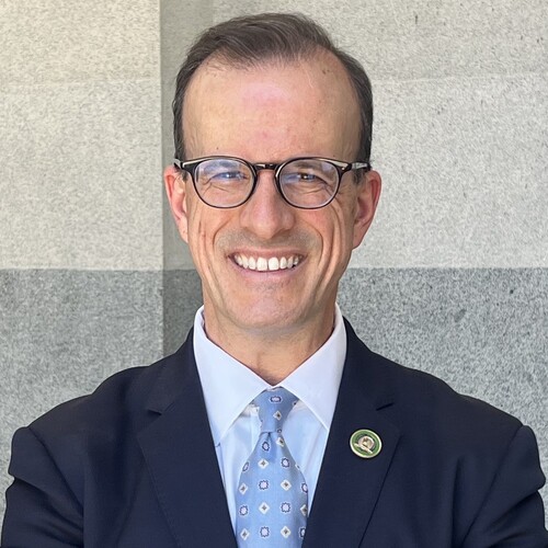 Marc Berman smiling in a professional headshot, wearing glasses and a navy suit with a light blue tie